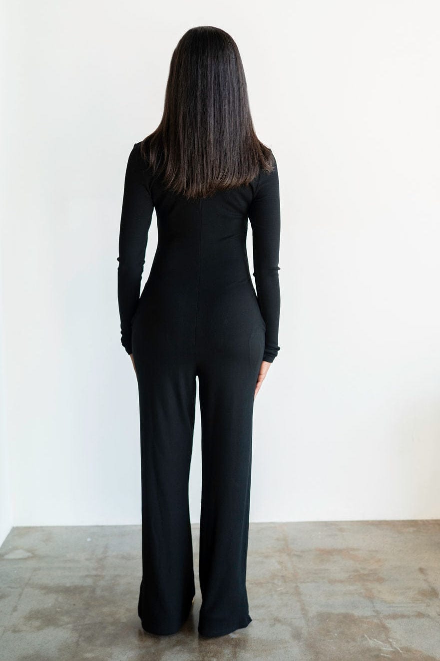 Person wearing a black outfit standing against a white wall.