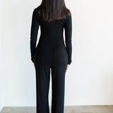Person wearing a black outfit standing against a white wall.
