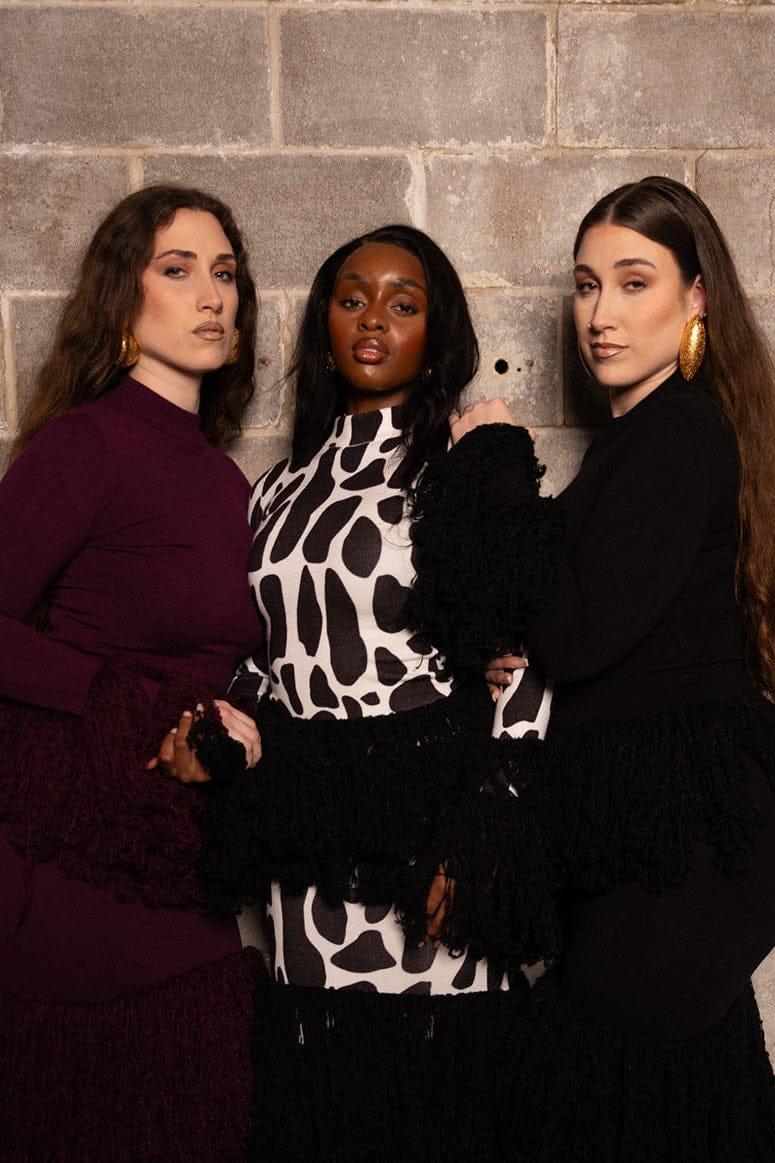 Three women posing together against a brick wall.